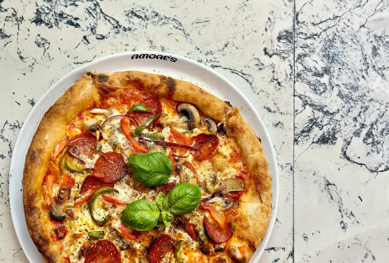 Freshly baked pizza topped with cheese, pepperoni, mushrooms, peppers and basil on a white plate.