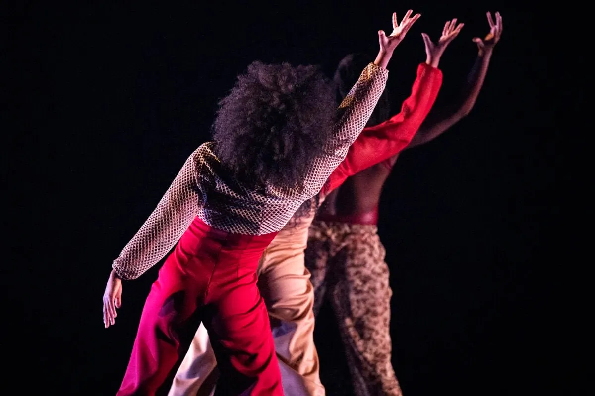 Performers in vibrant costumes dance on stage with arms raised during a theatrical production.
