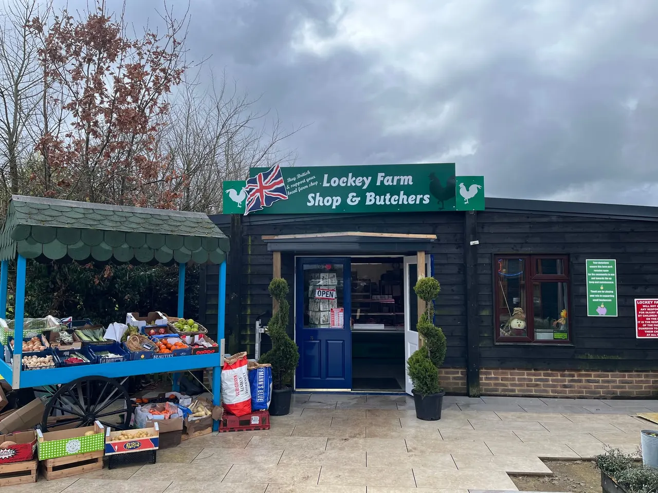 Farm shop storefront with produce display outside on a blue-framed stand under a green awning.