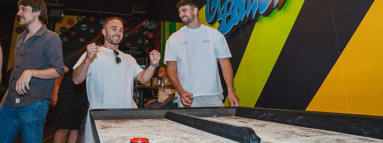 Three men playing shuffleboard indoors at a leisure venue with colourful wall graphics.