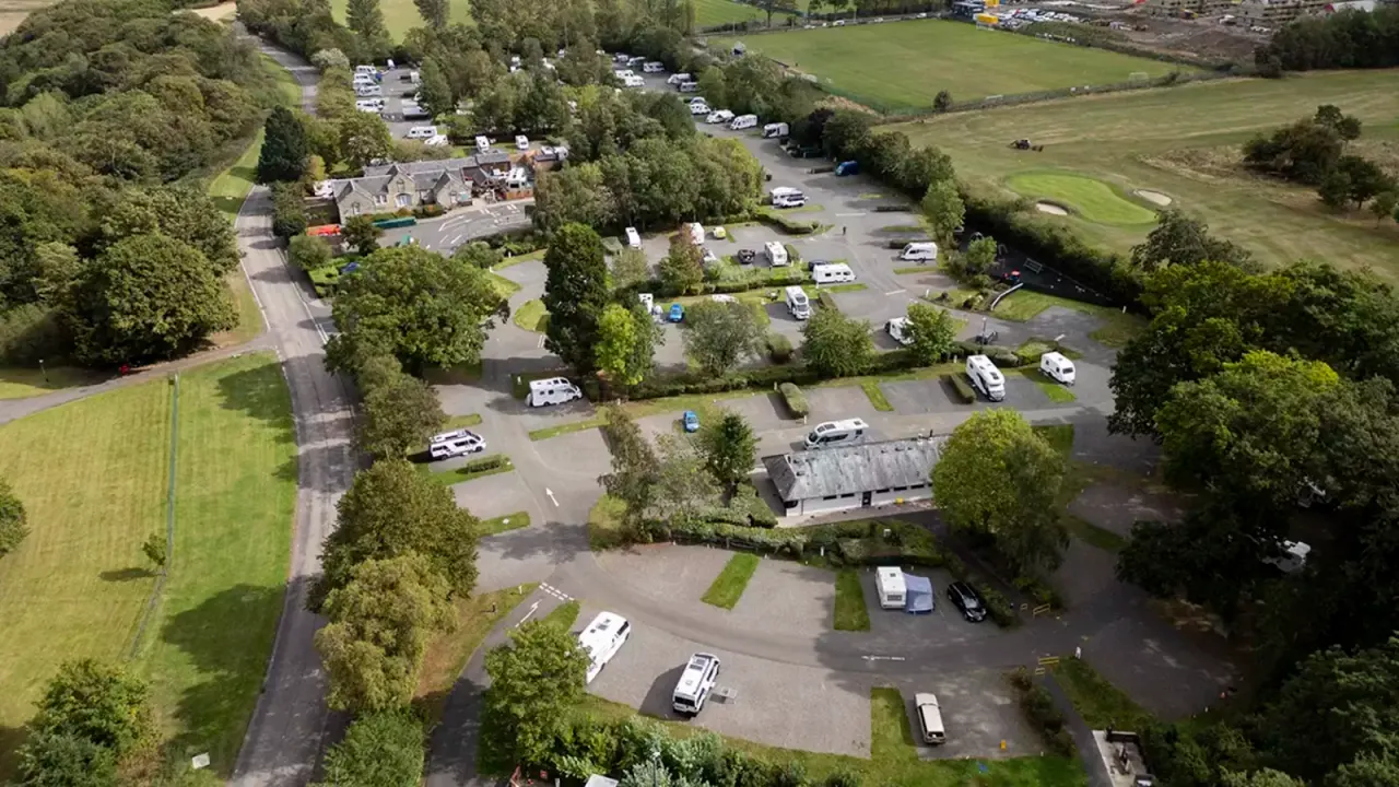 Aerial view of a countryside campsite with caravans and motorhomes parked in designated areas surrounded by trees and green fields.