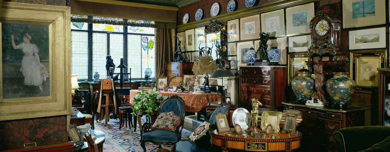Interior of a Victorian artist's studio filled with paintings, decorative plates, sculptures, antique furniture and ornamental objects.
