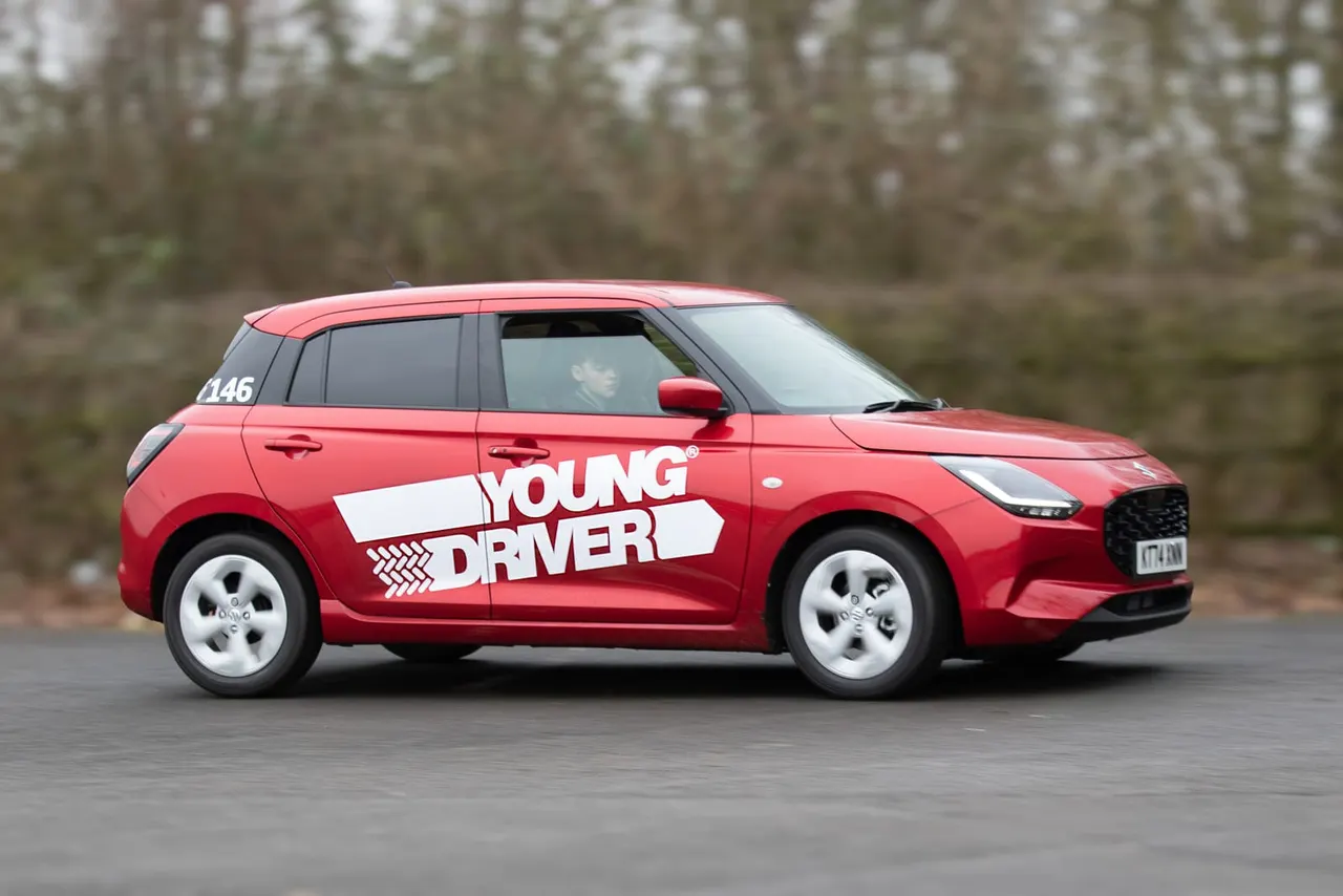 Red car with 'Young Driver' branding parked on asphalt with evergreen woodland in background.