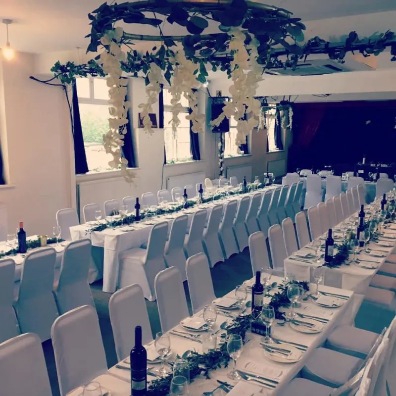 Elegant banquet hall with long tables set for a formal event, white chairs, place settings, and hanging floral decorations.