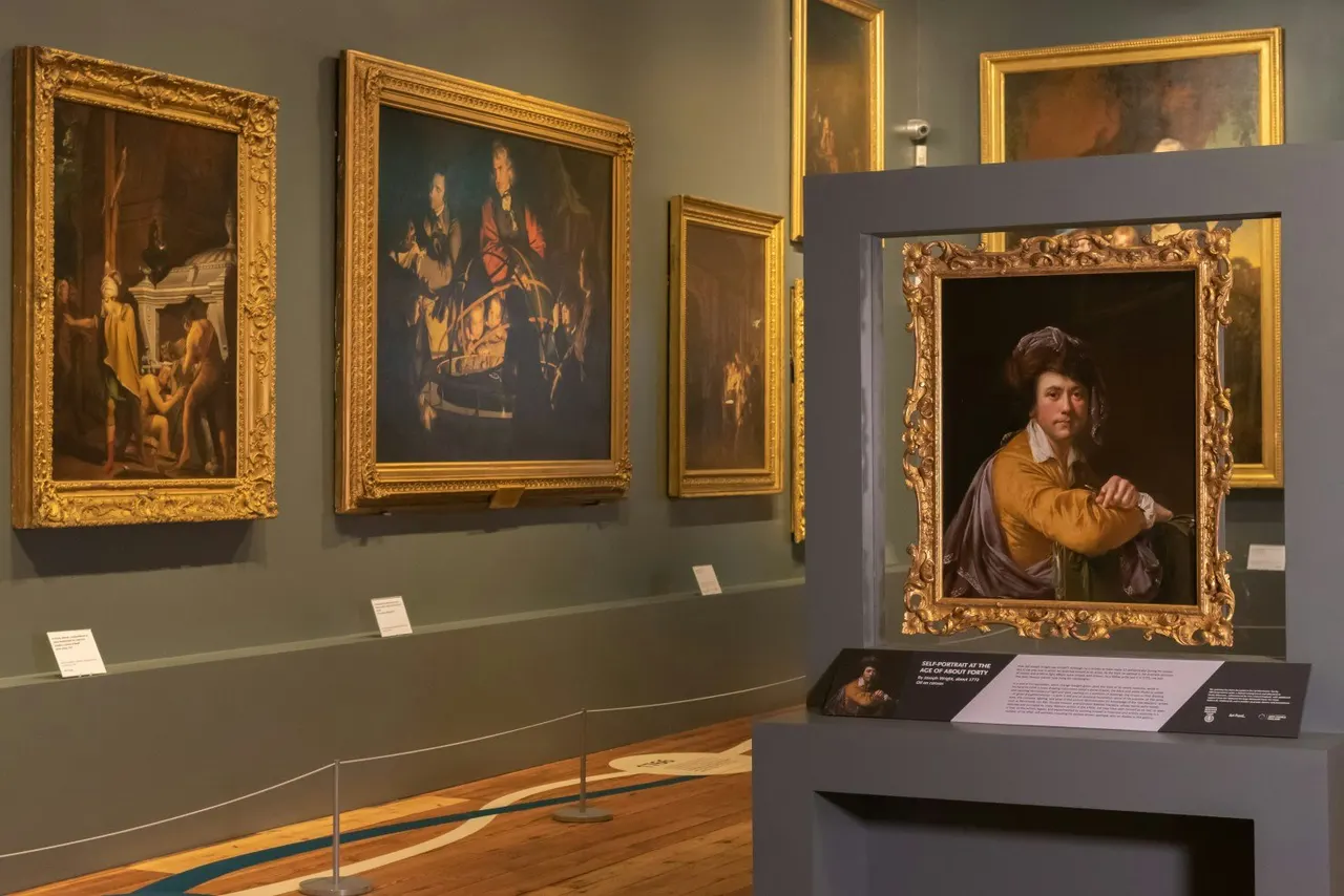 Gallery room displaying old master paintings in ornate gilt frames hung on sage-green walls, with a portrait in a separate display case.