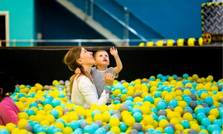 Two young children playing in a ball pit filled with yellow and blue balls, looking upward.