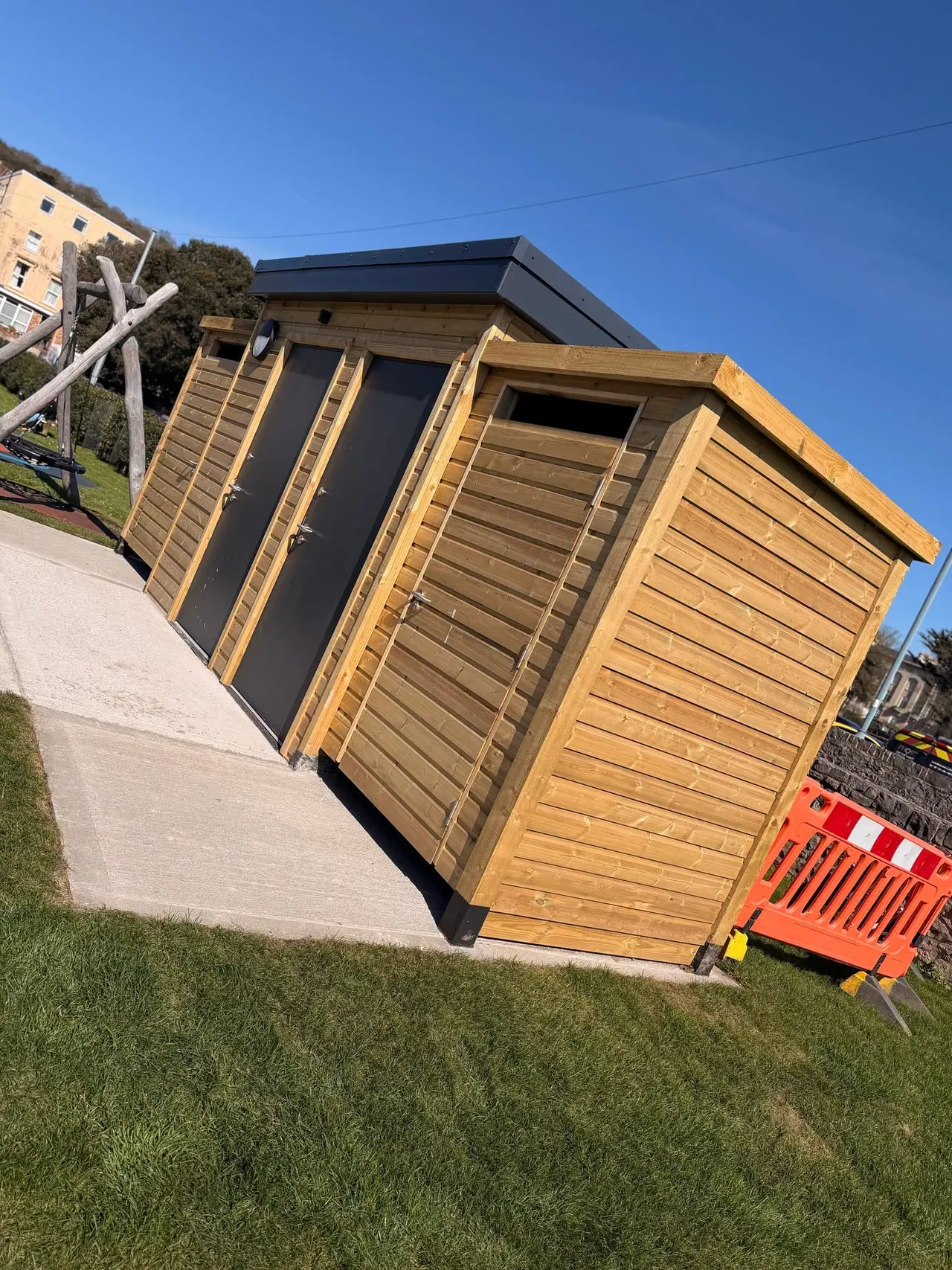 This is a PHOTOGRAPH.

Wooden glamping pods with black doors on a grassy area under clear blue sky.