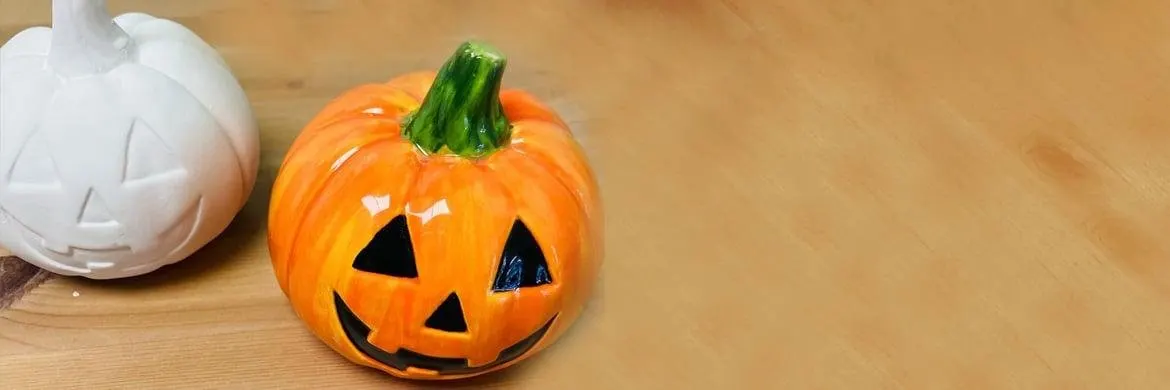 Two ceramic jack-o'-lantern decorations on a wooden surface, one orange with a carved face and one white.