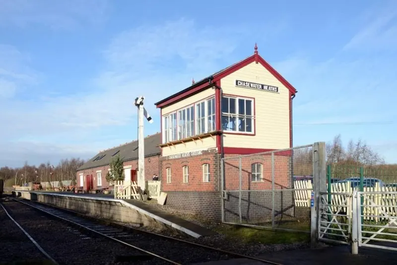 Historic railway signal box and station building beside railway tracks on a clear day.