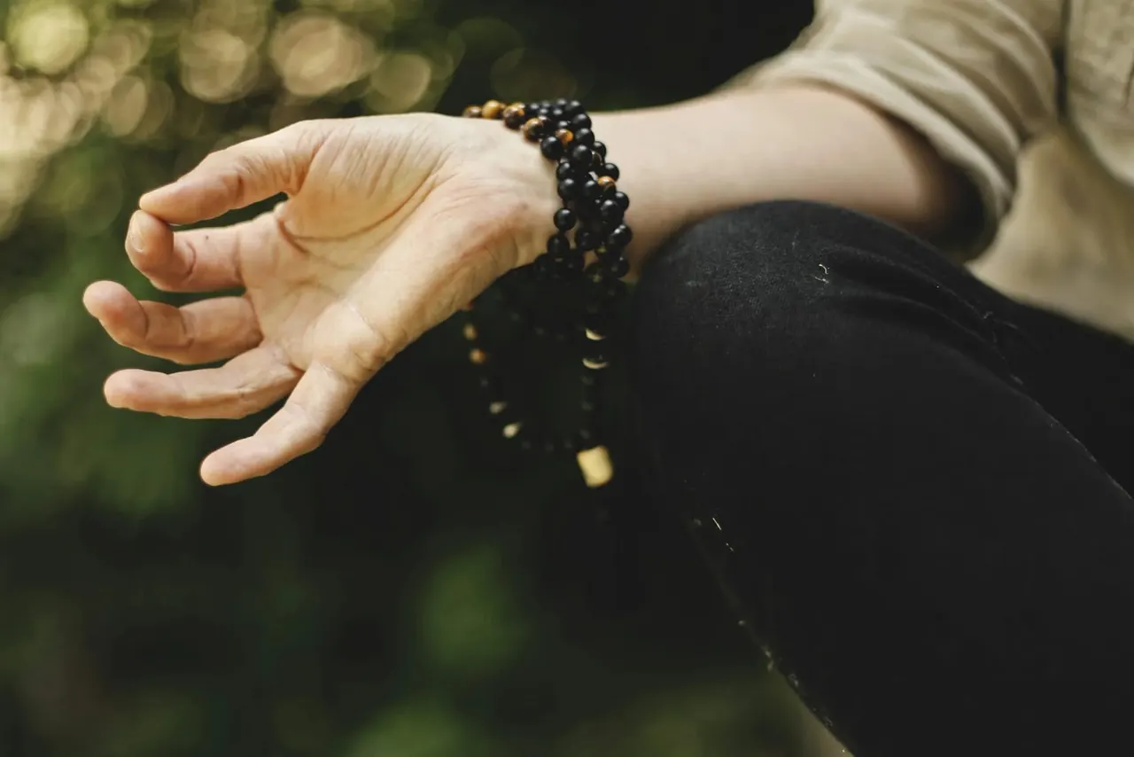 Person's hand holding a beaded bracelet with berries falling from it in a garden setting.