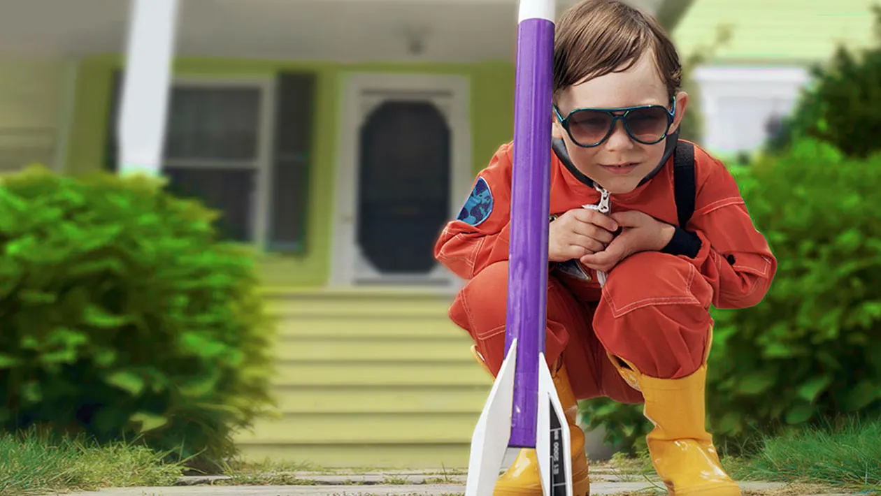 Young child in red jacket and sunglasses holding a large purple and white pole outdoors.