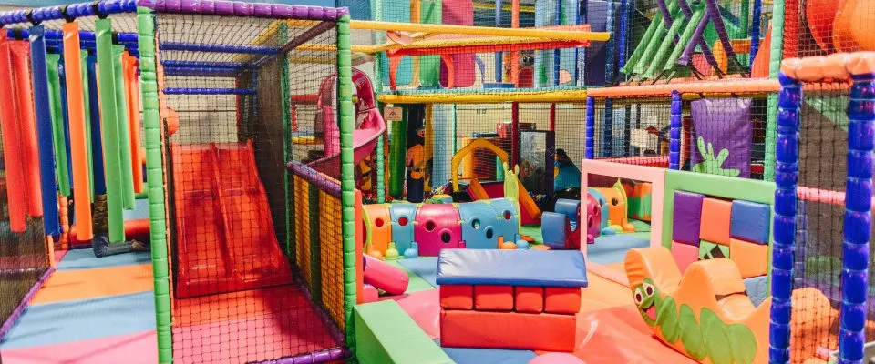 Colourful indoor play area with soft structures, foam blocks, slides and climbing frames for young children.