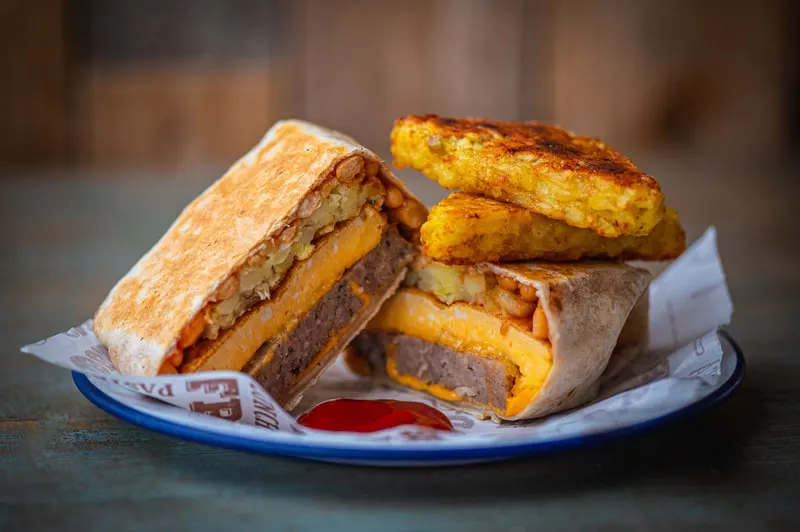 A toasted sandwich and golden fried potato cakes served on a paper-lined plate.