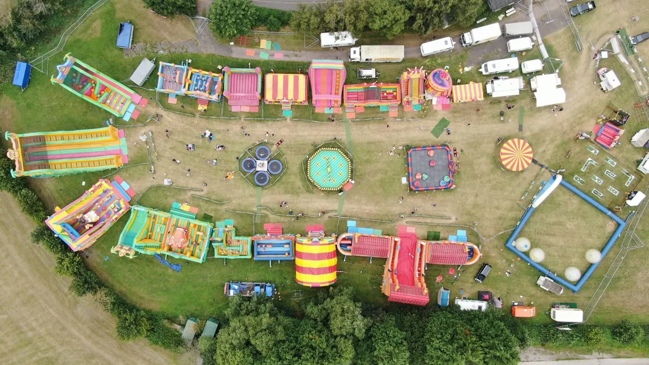 Aerial view of an inflatable theme park with colourful bouncy castles, slides and assault courses arranged across a grass field.