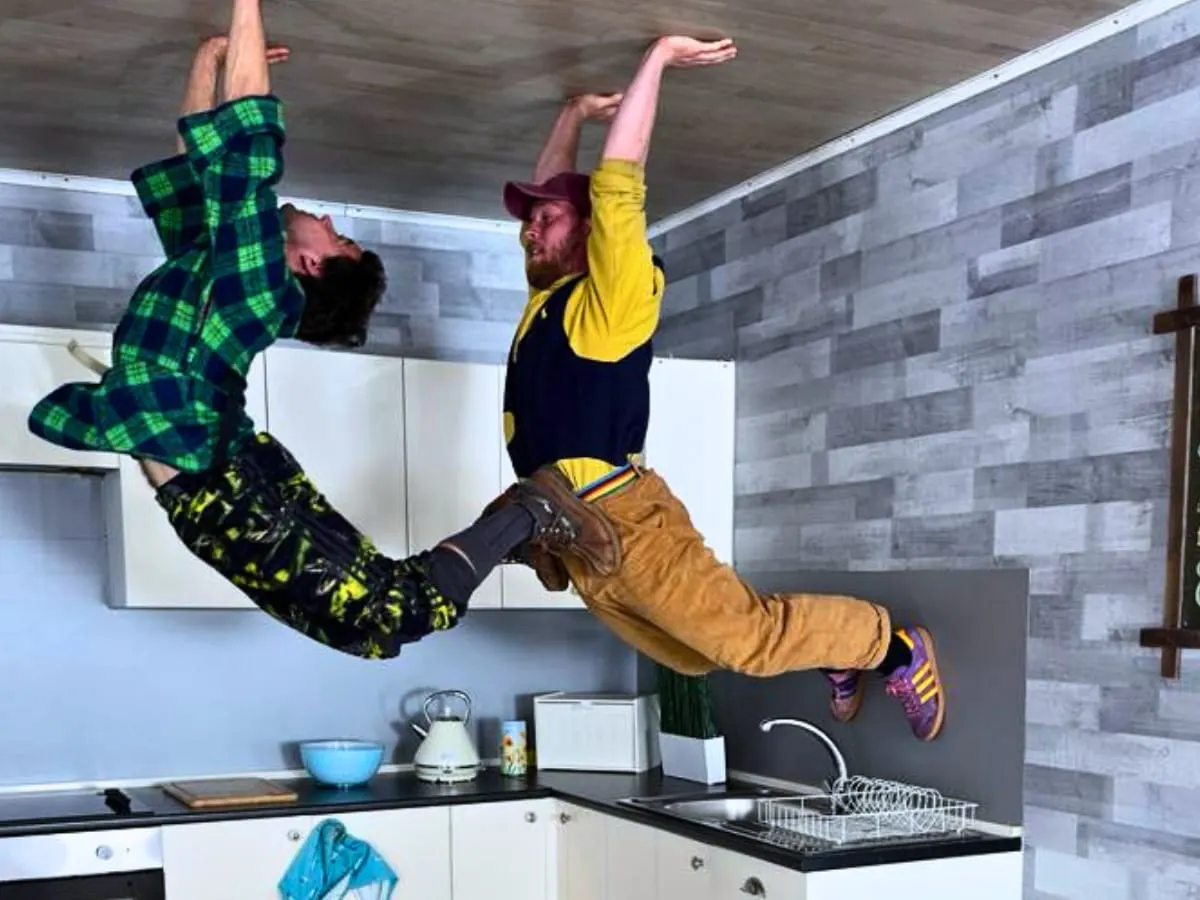 Two people floating upside down in an inverted kitchen with appliances and countertops on the ceiling.