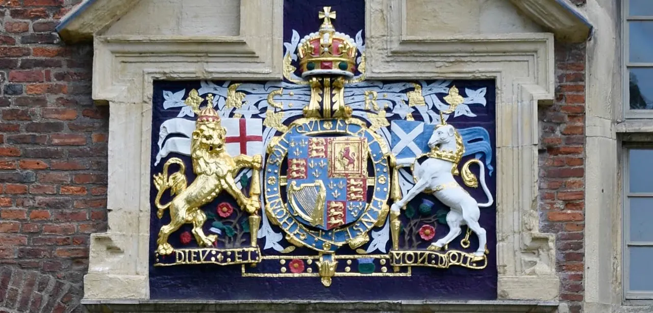 Ornate heraldic coat of arms mounted on a stone building facade, featuring a crowned shield with gilt lion and unicorn supporters.