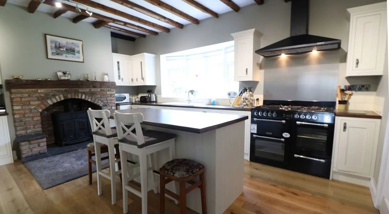 This is a PHOTOGRAPH.

Modern kitchen with central island, black range cooker, white cabinetry, and a brick fireplace with wood-burning stove in the background.