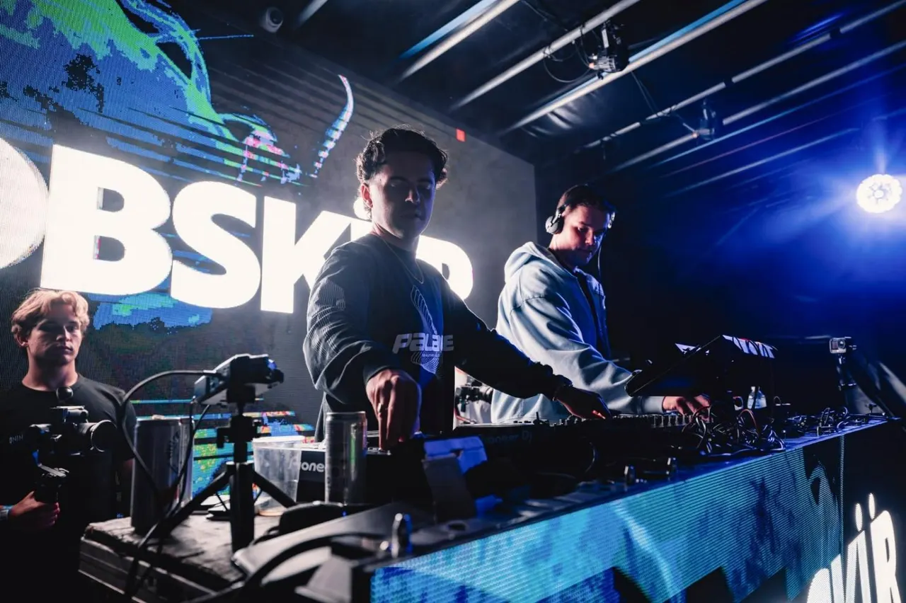DJs performing at a nightclub with blue lighting, large screens, and electronic music equipment on stage.