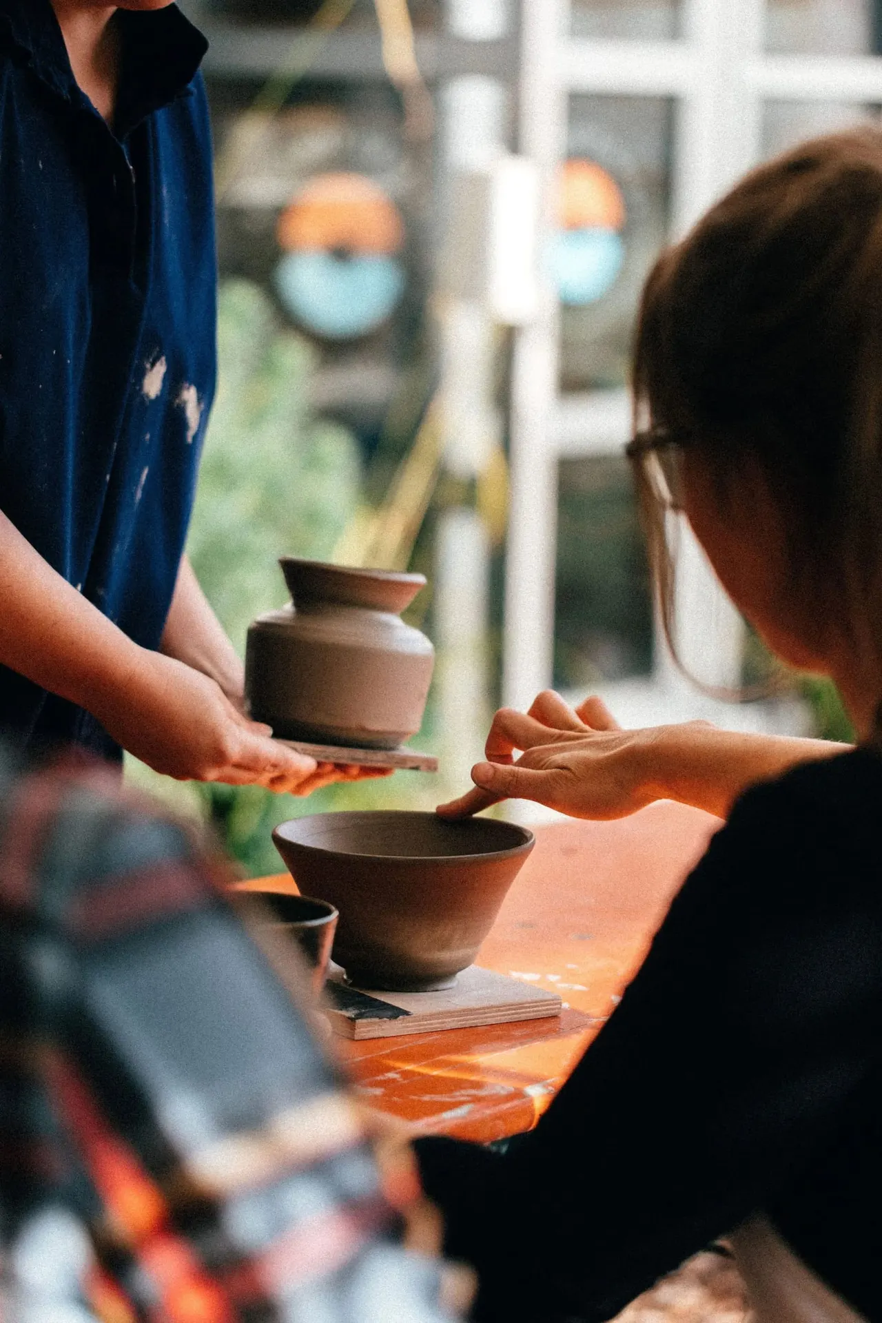Two people handling ceramic bowls at a pottery workshop table during a hands-on class.