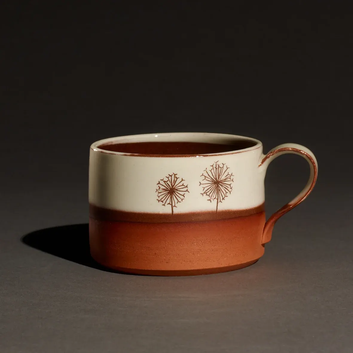 Ceramic mug with cream and terracotta glaze featuring hand-drawn dandelion designs.