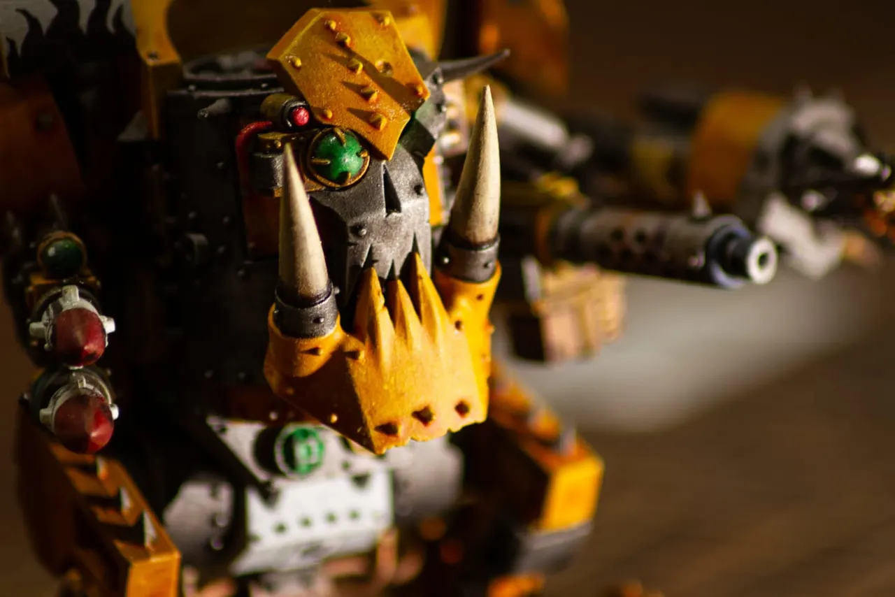 Close-up of a yellow and black fantasy figurine with horns and glowing green eyes among other miniature gaming pieces.