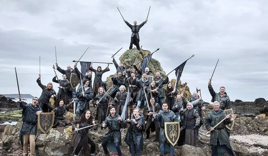 Large group of people in medieval costume and armour posing with weapons on a rocky hilltop.