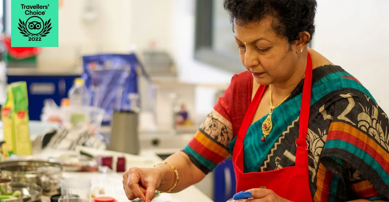 Woman in colourful patterned clothing and red apron preparing food at a cooking school workstation.