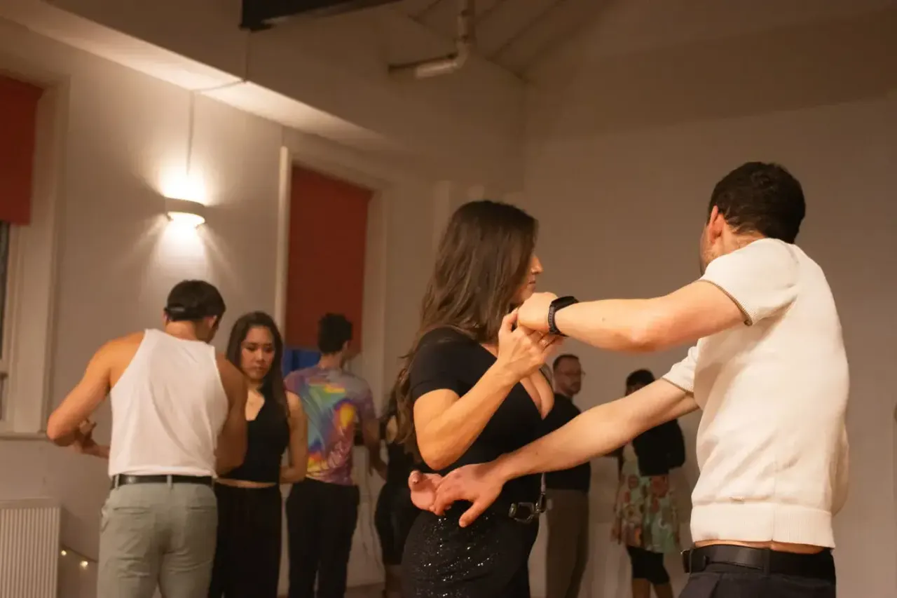A group of people dancing together indoors during a salsa class, with couples practising moves in a studio space.
