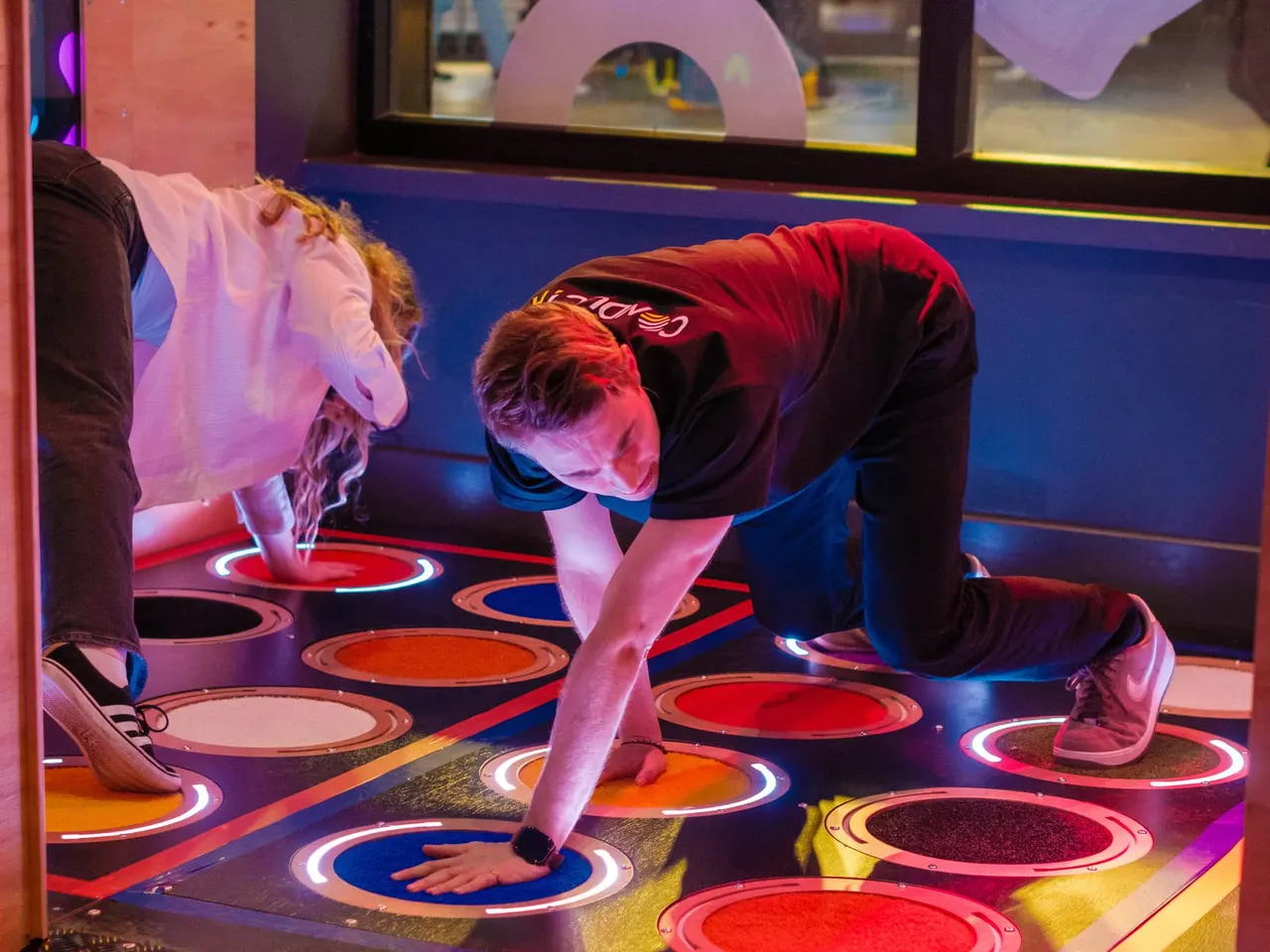 Child playing on an interactive illuminated floor game with colourful lit panels whilst other visitors stand nearby.