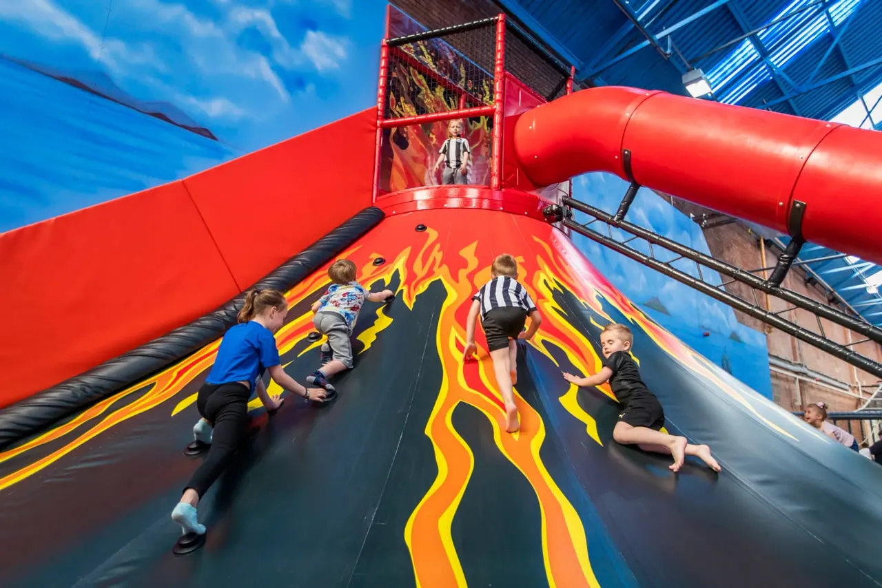 Children sliding down a large inflatable slide with red tubing and flame graphics at an indoor play centre.