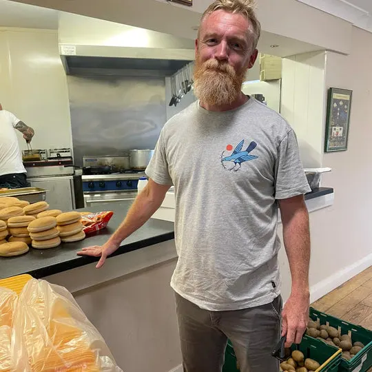 Man standing in kitchen with baked goods on counter and fresh produce in crates.