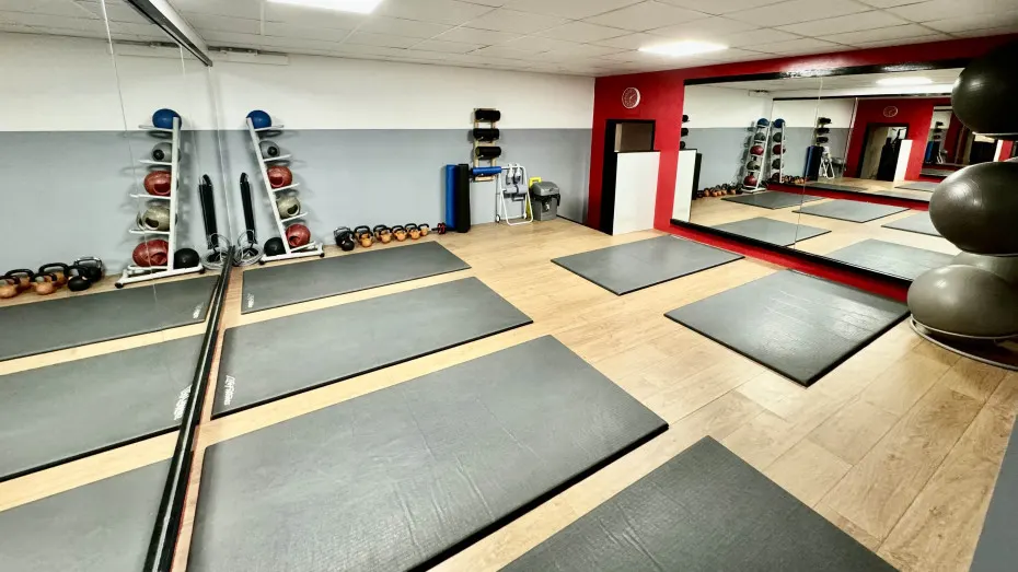 Spacious gym studio with exercise mats, dumbbells, stability balls, and mirrored walls for fitness classes.