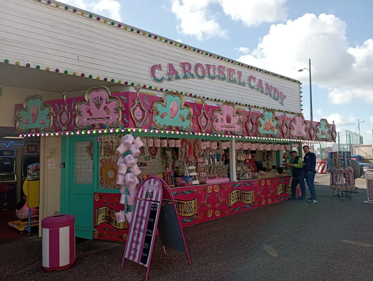 Colourful carousel candy stall with pink and green decoration, candy floss display, and fairground merchandise at an amusement park.