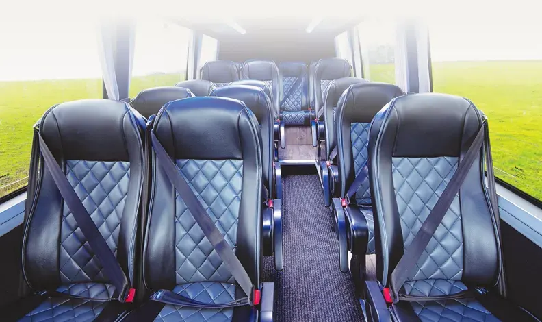 Interior of a coach with rows of blue and black quilted seats facing forward, green fields visible through windows.