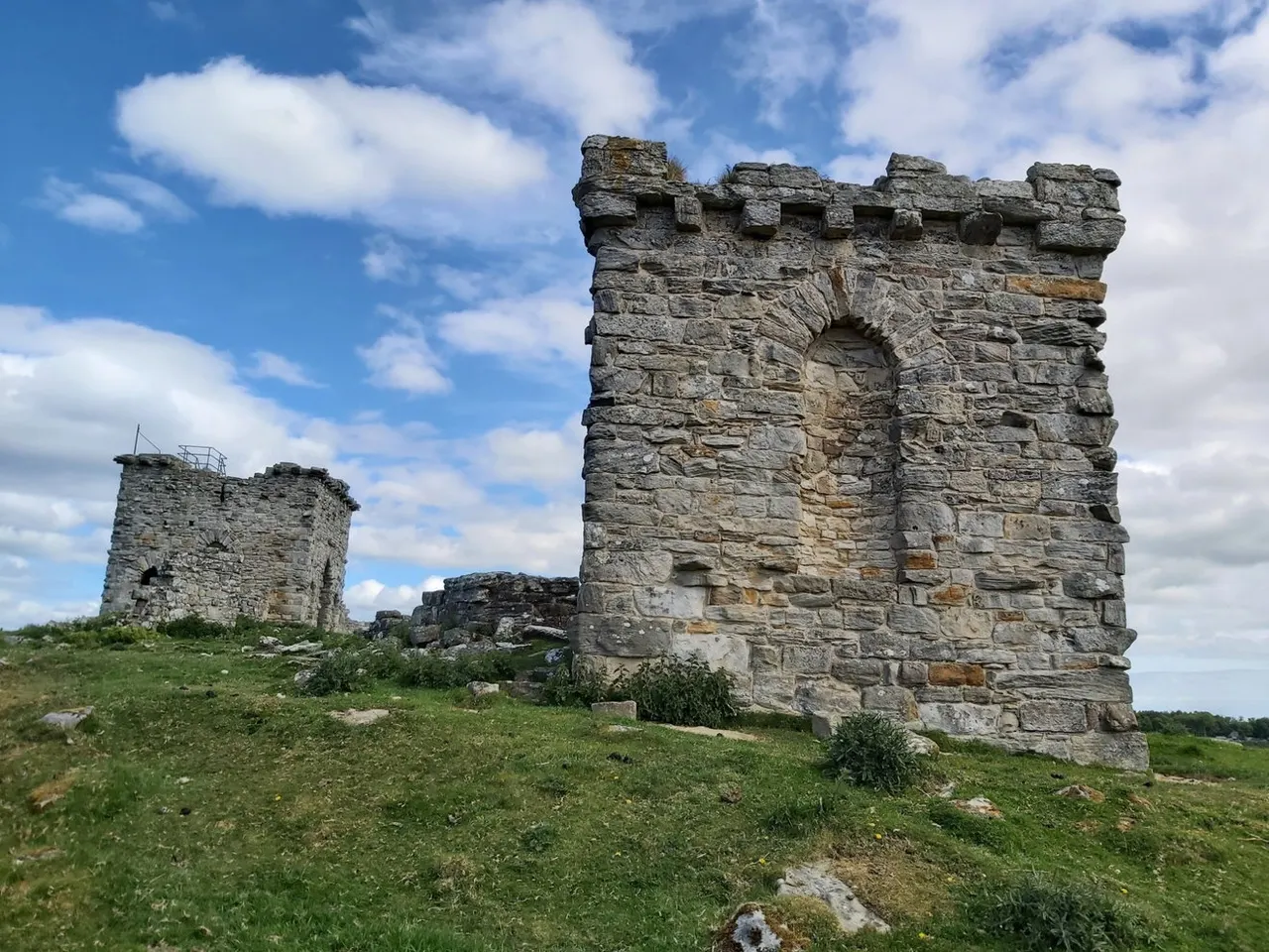Ruins of a medieval stone castle with crenellated towers standing in a grassy field under blue sky.