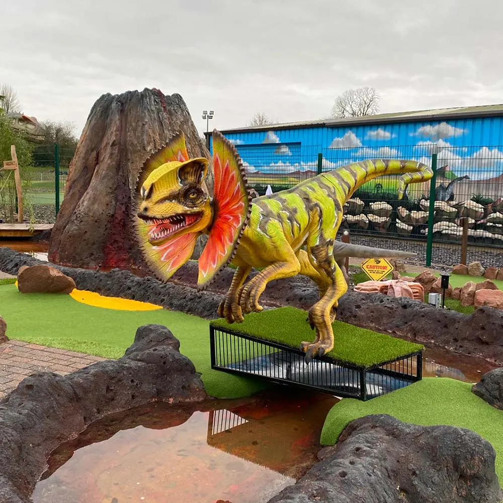 Colourful dinosaur sculpture on a mini golf course with artificial turf, rocks, and a small bridge over water.