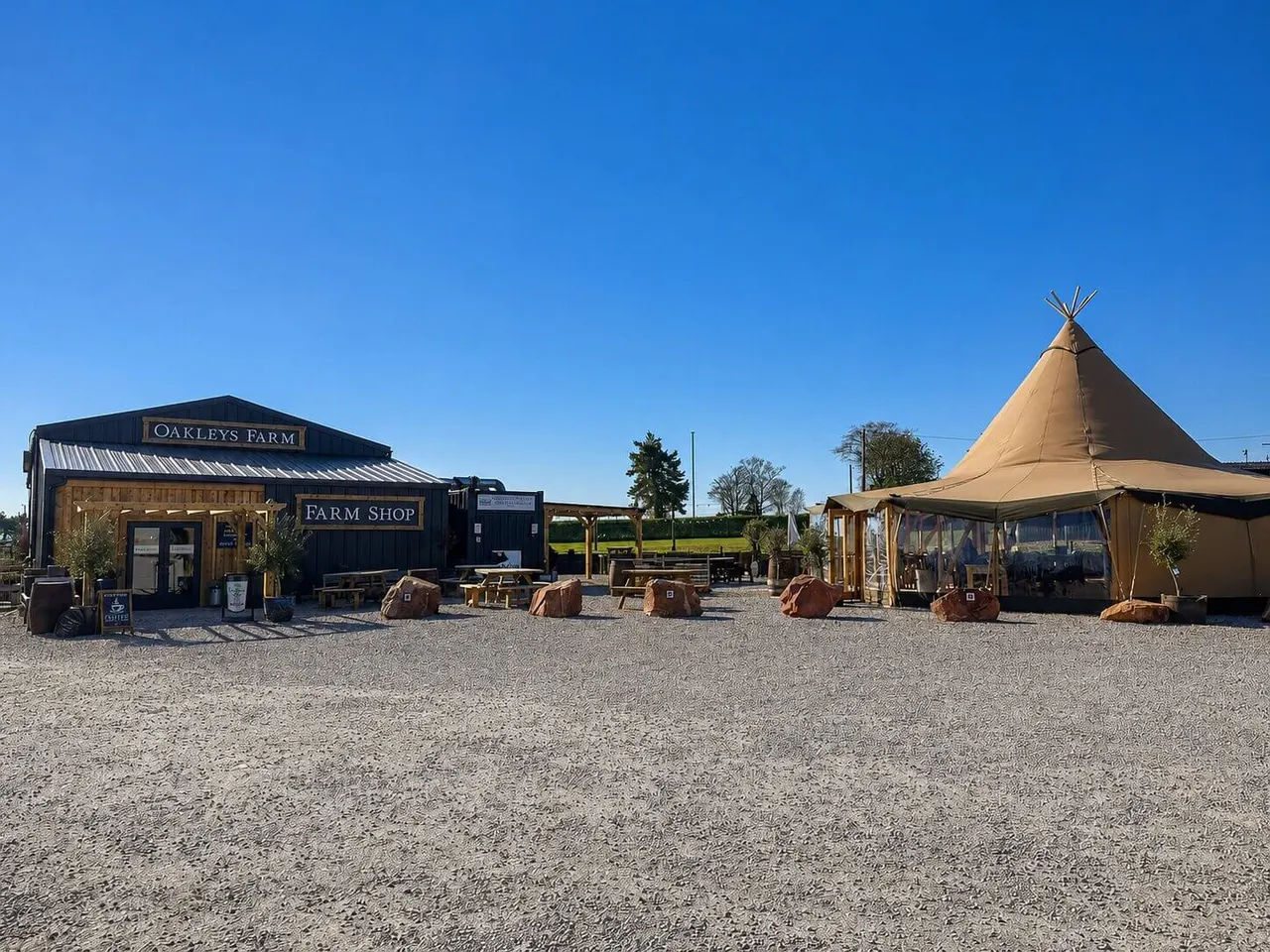 Farm shop and outdoor recreational buildings with a large tipi tent in a rural setting under clear blue sky.