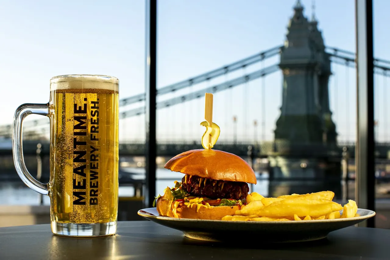 A pint of lager and a burger with chips on a table overlooking Tower Bridge in London.