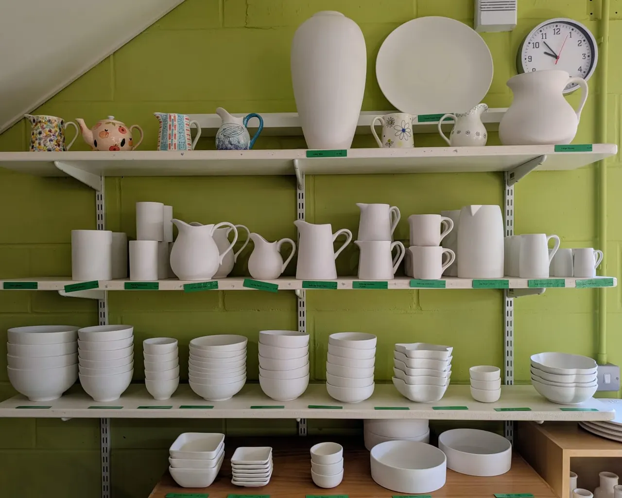 White ceramic tableware and decorative pieces displayed on shelves against a bright lime-green wall.
