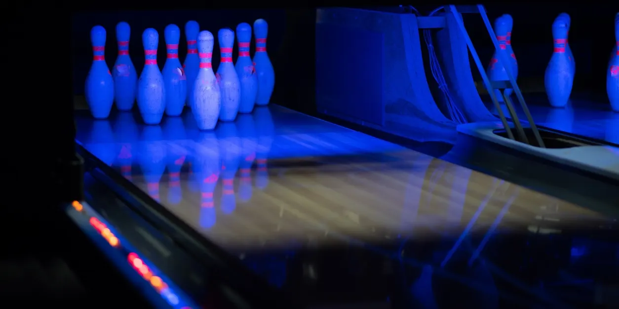 Blue neon-lit bowling pins set up on a lane with a bowling ball ready to roll.