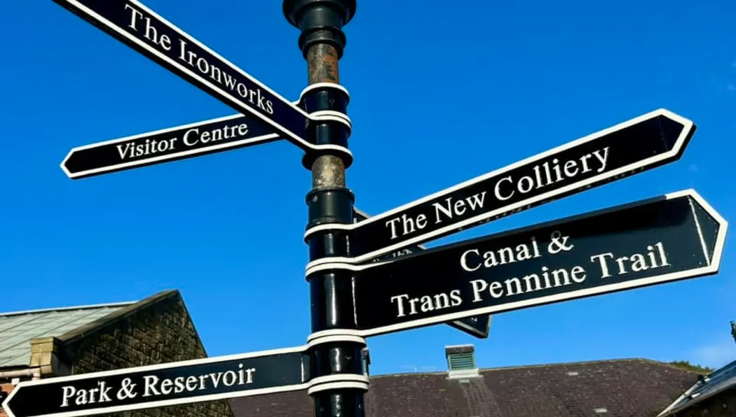 Directional sign post with multiple black and white arms pointing to local attractions including The Ironworks, Visitor Centre, The New Colliery, and Canal & Trans Pennine Trail.