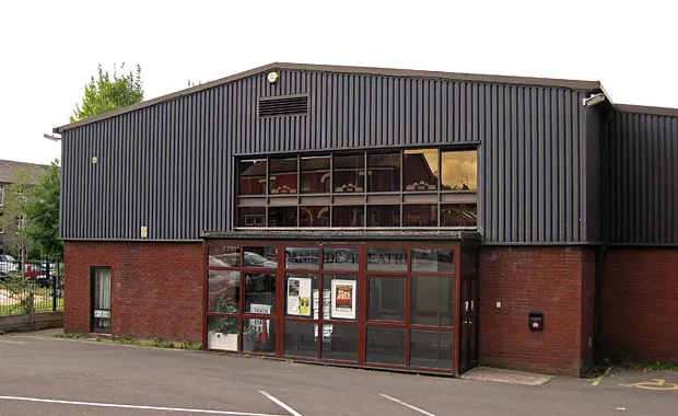 Modern brick and corrugated metal theatre building with red entrance doors and display windows.