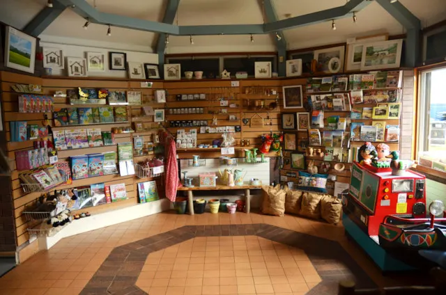 Interior of a circular gift shop and visitor centre with wooden walls lined with books, crafts and postcards.
