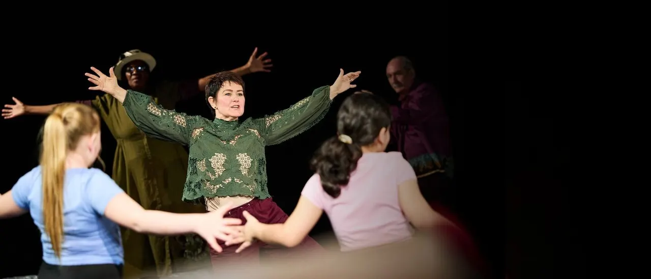 Actors perform an interactive theatre scene with children on stage, engaging them with expressive gestures and movement.