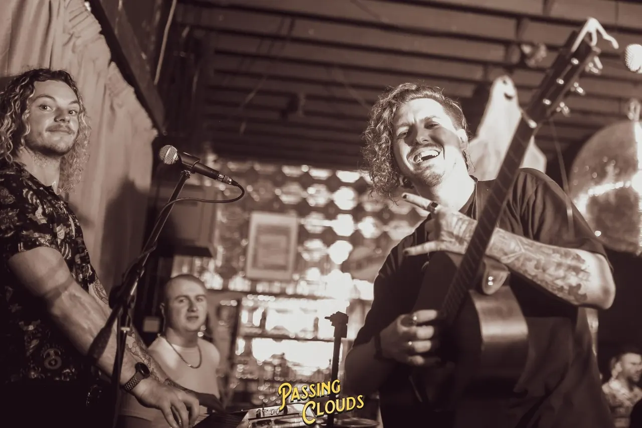 Band performing on stage indoors with audience members watching and smiling.