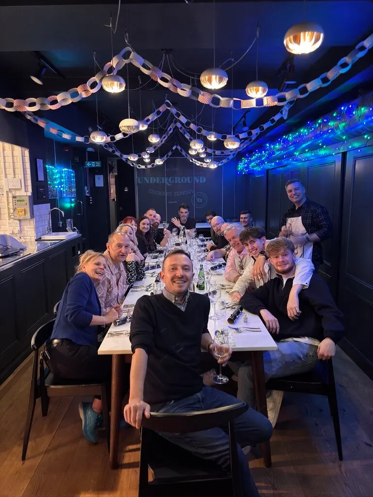 A group of diners seated at a long table in a dimly lit restaurant with decorative chain lighting overhead.