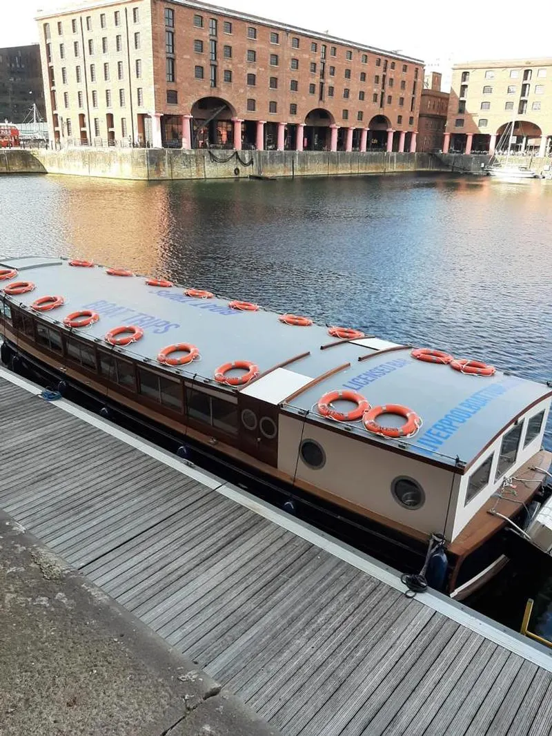 Tourist boat moored at a dock with life rings on deck, historic warehouse buildings across the water.