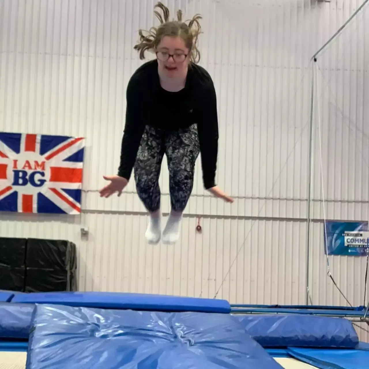Young person bouncing on a trampoline in an indoor gymnastics facility with blue padding and safety netting.