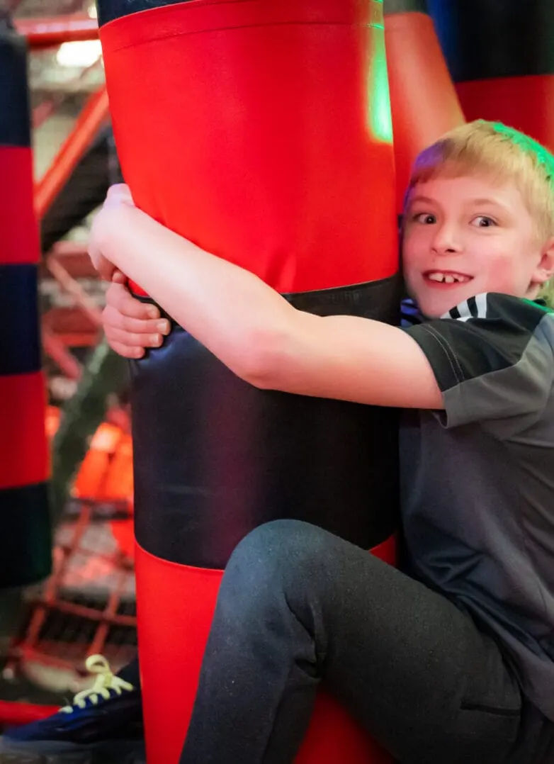Young child hugging a large red and black inflatable pillar inside an indoor play facility.