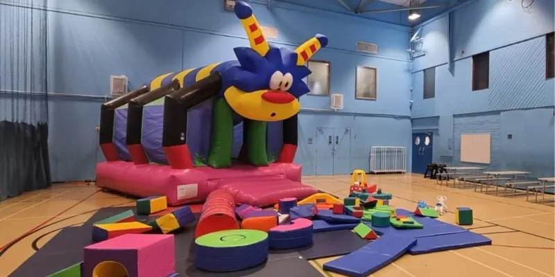 Colourful inflatable play structure and soft play equipment set up in a sports hall.